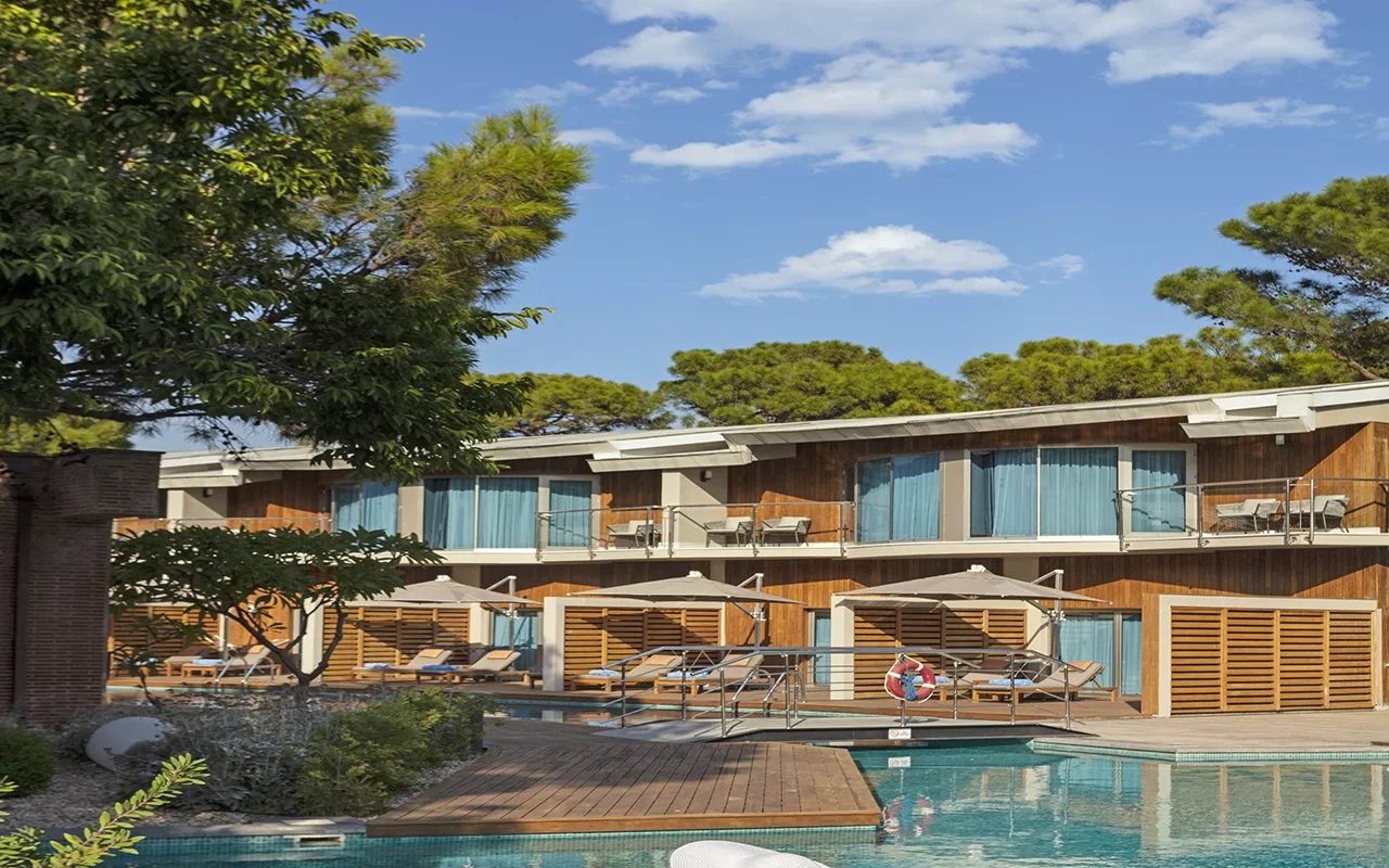Garden villas with private terraces around a pool, framed by pine trees